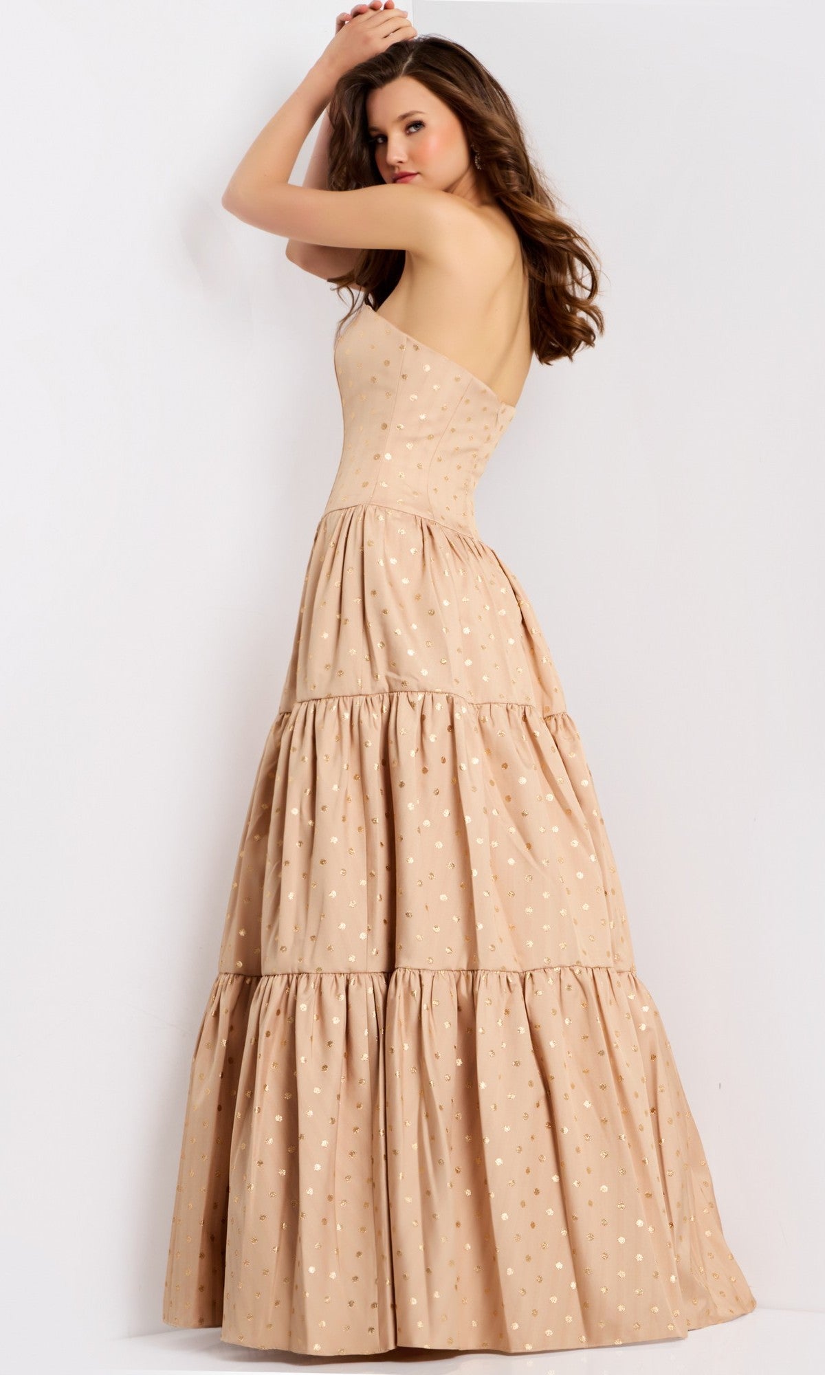 A woman poses against a plain background in the Jovani 49341 long prom dress—strapless, beige, floor-length, with a tiered skirt and subtle polka dot pattern.